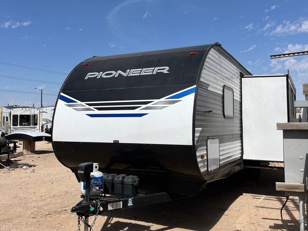 Black and white Pioneer travel trailer with blue accents parked on dirt under blue sky.
