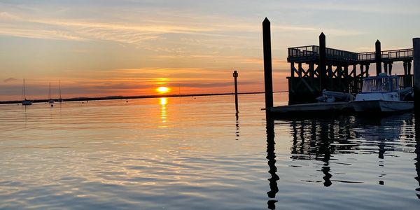 Sunset over calm waters with boats docked at a pier.