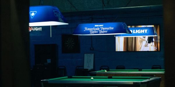 Dimly lit pool hall with blue Bud Light lights and a dartboard on the wall.