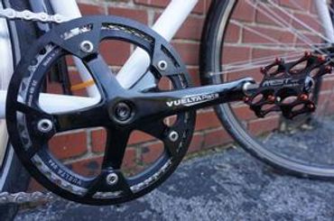 Close-up of a bicycle crankset and pedal against a brick wall.