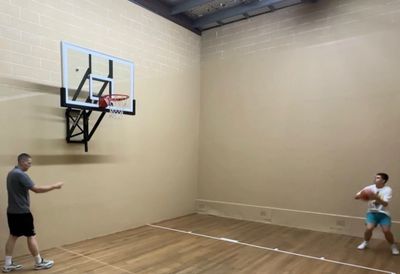 Two people playing basketball in an indoor court with a small hoop.