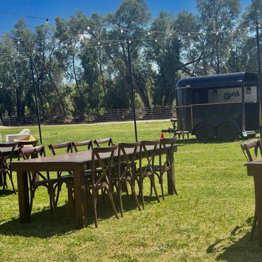 Outdoor wooden tables and chairs set on grass with string lights overhead.