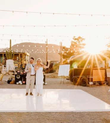 Couple celebrating at outdoor sunset event with string lights and vintage decor.