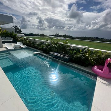 Modern pool with clear water and a pink flamingo float under a cloudy sky.