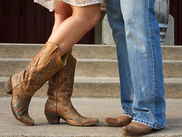 A couple wearing cowboy boots stand close together on concrete steps.