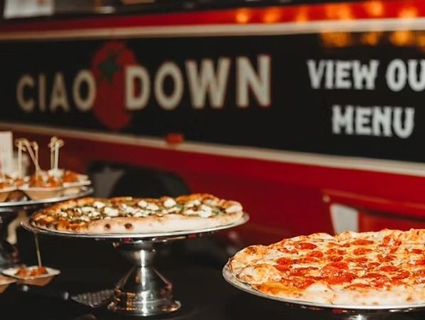 Two pizzas displayed on stands in a restaurant with a sign in the background.