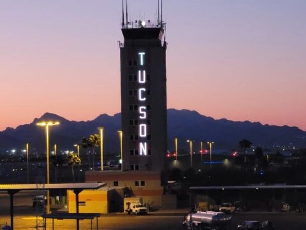Tucson airport control tower illuminated at dusk with mountains in background.