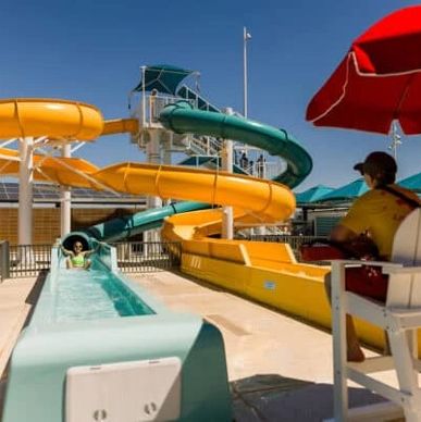 A child slides down a yellow water slide while a lifeguard watches.
