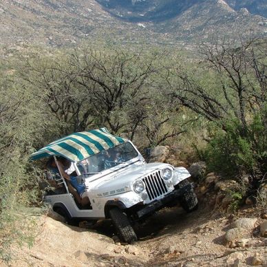 White jeep navigating a rocky, rugged trail in a desert landscape.
