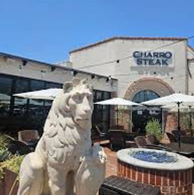 Stone lion statue at Charro Steak restaurant patio with umbrellas.