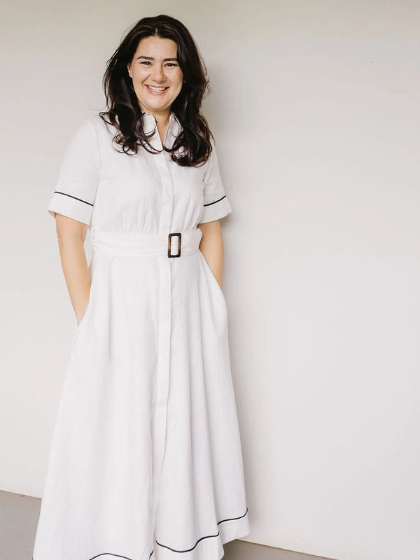 Woman in a long white dress with pockets and black trim, smiling.