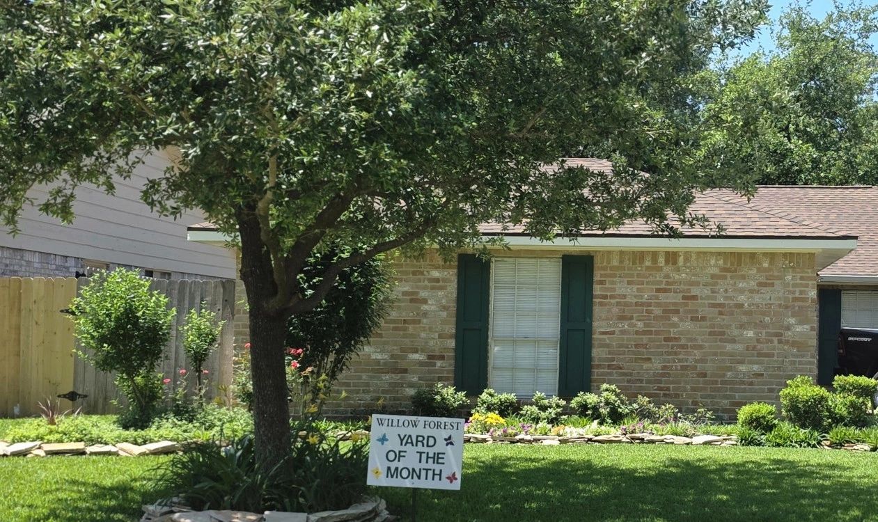 A well-maintained yard with a "Yard of the Month" sign in front of a brick house.