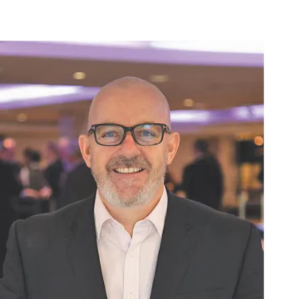 Smiling bald man with glasses in a suit at an indoor event.