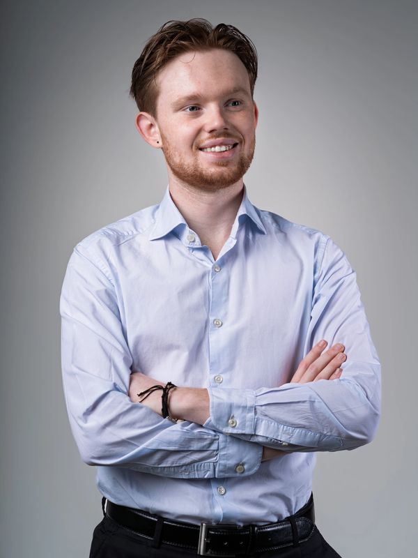 Confident young man with red hair and beard, smiling with arms crossed.