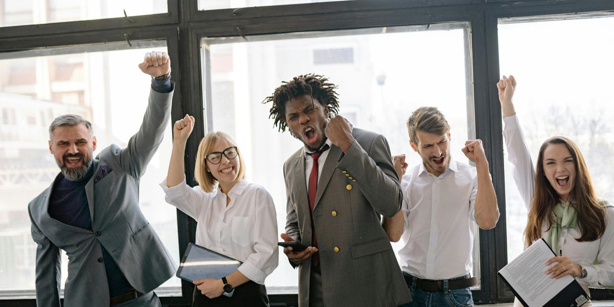 Group of diverse professionals celebrating success with raised fists indoors.