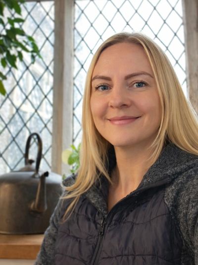 A smiling woman with blonde hair in a cozy room with lattice windows.