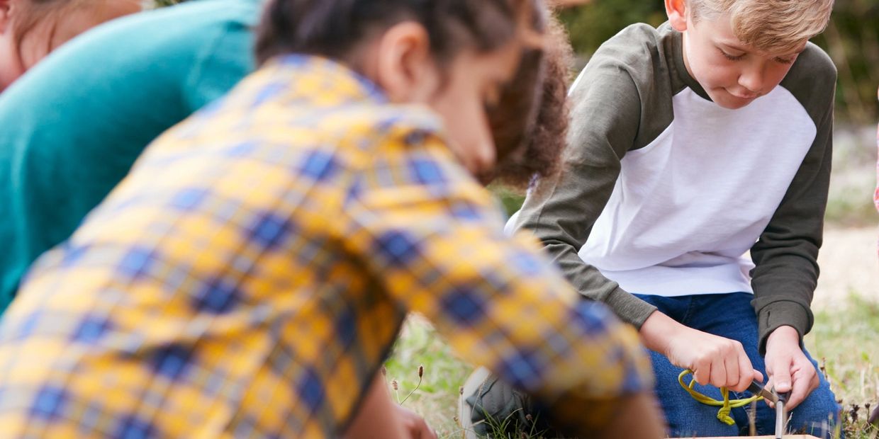 Boy using a tool while two kids watch.