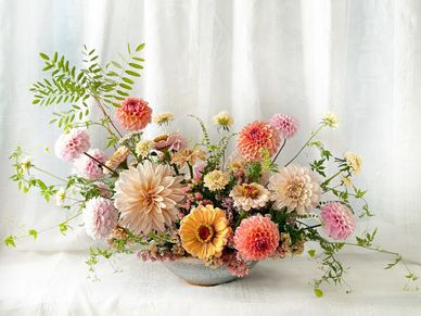 Elegant pastel floral arrangement in a shallow bowl with soft greenery.