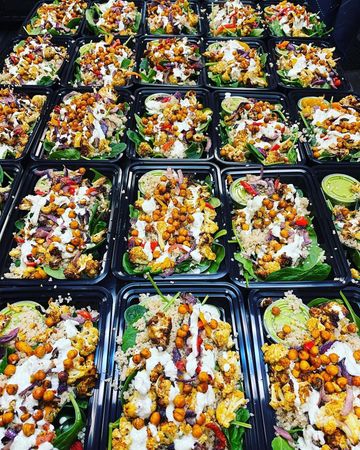 Multiple meal prep containers with roasted chickpeas, cauliflower, spinach, quinoa, and creamy dressing.