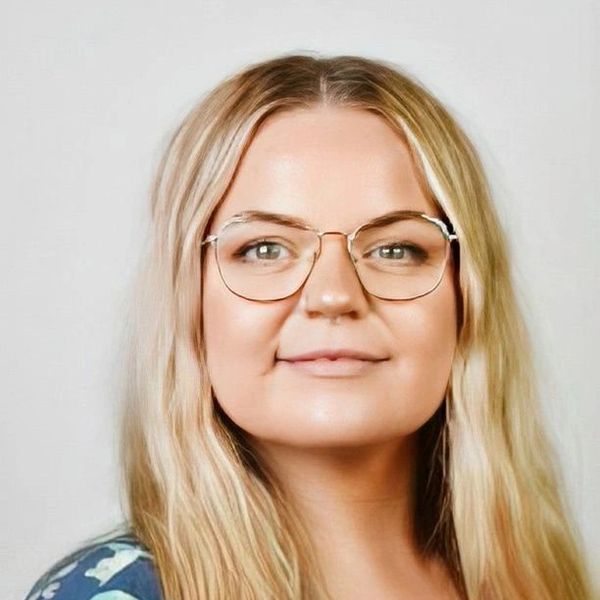 Portrait of a woman with blonde hair and glasses smiling gently.