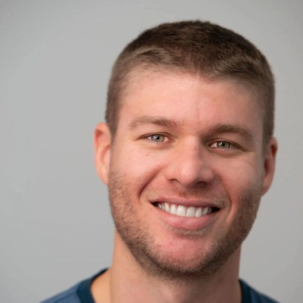 Smiling young man with short hair and light beard against a plain background.