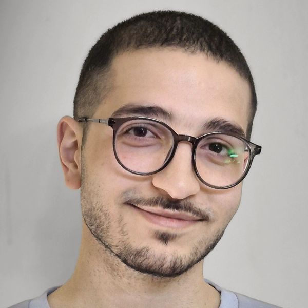Young man with round glasses smiling gently at the camera.