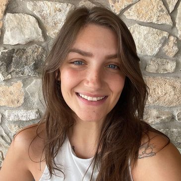 Smiling woman with long brown hair in front of a stone wall.