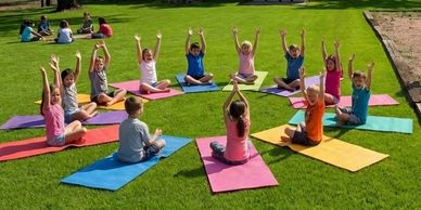 Children practicing yoga outdoors on colorful mats in a circle.