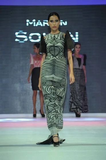 Model walking runway in a black and white patterned dress with sheer sleeves.