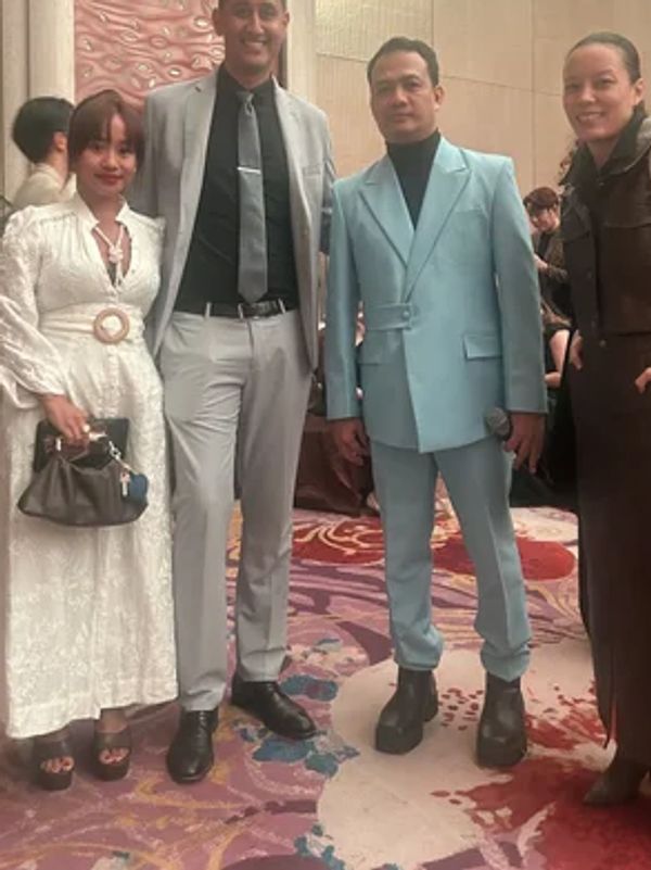 Four people dressed in formal attire posing indoors on a colorful carpet.