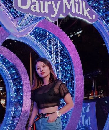 Young woman posing in front of a glowing Dairy Milk sign at night.