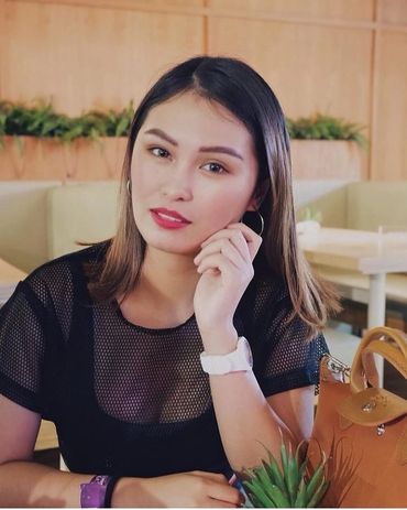Woman with shoulder-length hair sitting indoors, resting her face on her hand.