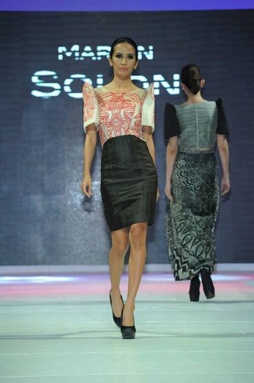 Model walks runway in a structured dress with a patterned top and black skirt.