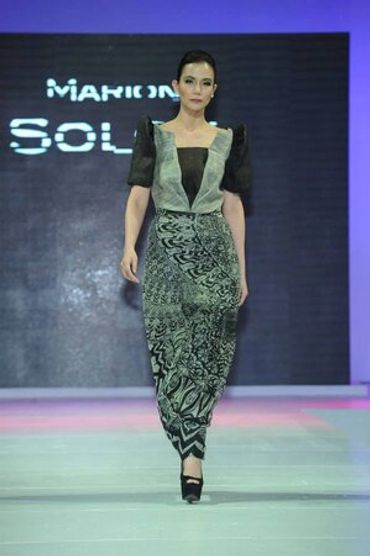 Model walking runway in a unique patterned dress with structured sleeves.