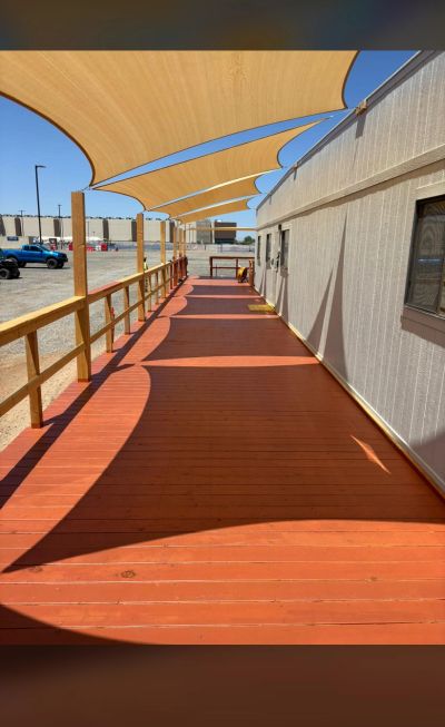 Outdoor shaded wooden walkway alongside a building on a sunny day.
