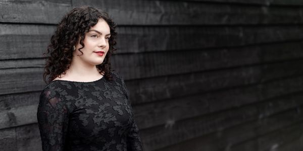 Woman with curly hair wearing a black floral lace dress.