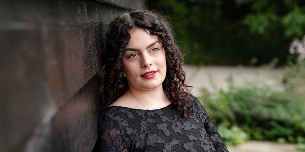 Woman with curly hair leaning against a wall outdoors.