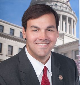 Man in suit smiling outdoors near a government building.