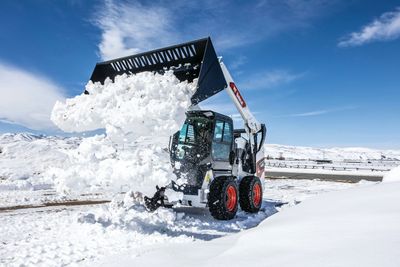 A Bobcat loader clearing snow on a bright winter day.