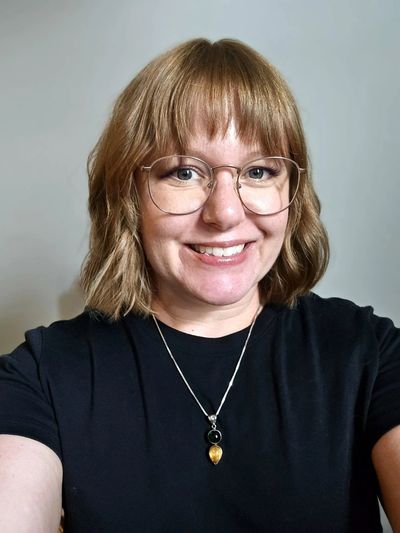 Smiling woman with glasses and shoulder-length hair.