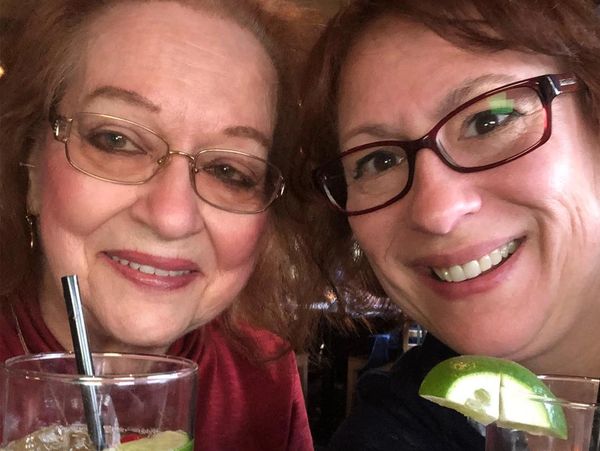 Two women smiling with drinks garnished with lime and cherry.