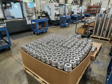 A large box filled with metal cylindrical parts in a manufacturing workshop.