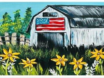 A barn with an American flag and yellow flowers in front under a blue sky.
