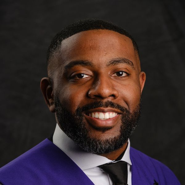 Smiling man in formal attire with purple graduation gown.