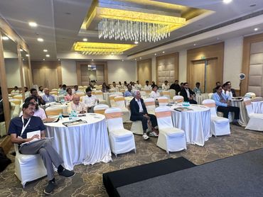 Attendees seated at round tables in a conference room with chandeliers.