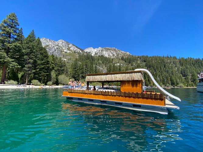 tiki boat with water slide on green water of Lake Tahoe with mountains in back