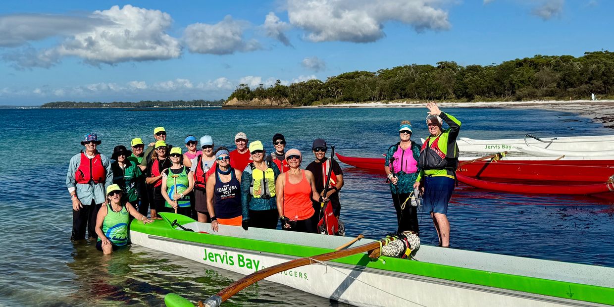 Group of people posing by canoes in a beach setting.