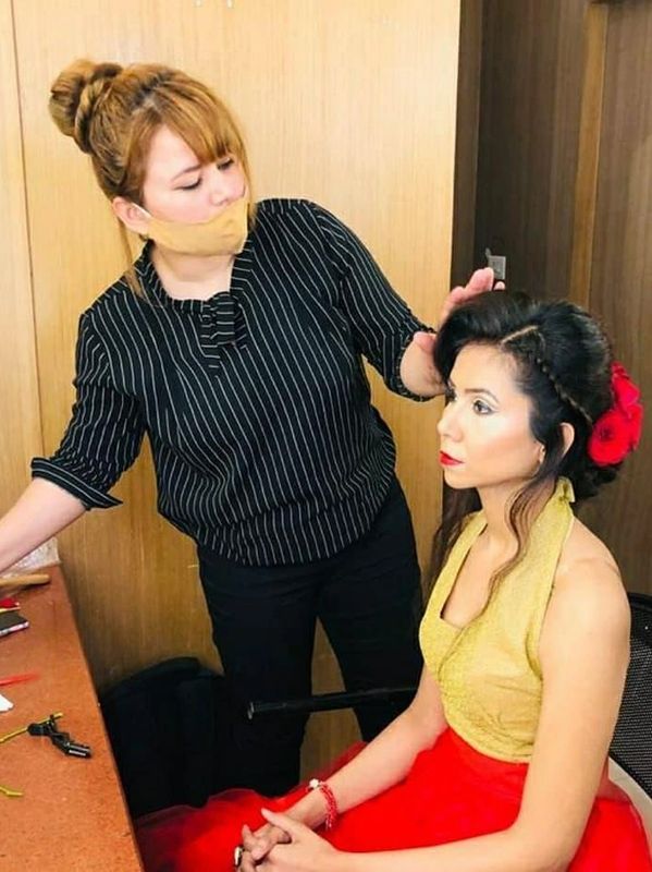 A stylist adjusts a woman's hair adorned with red flowers.