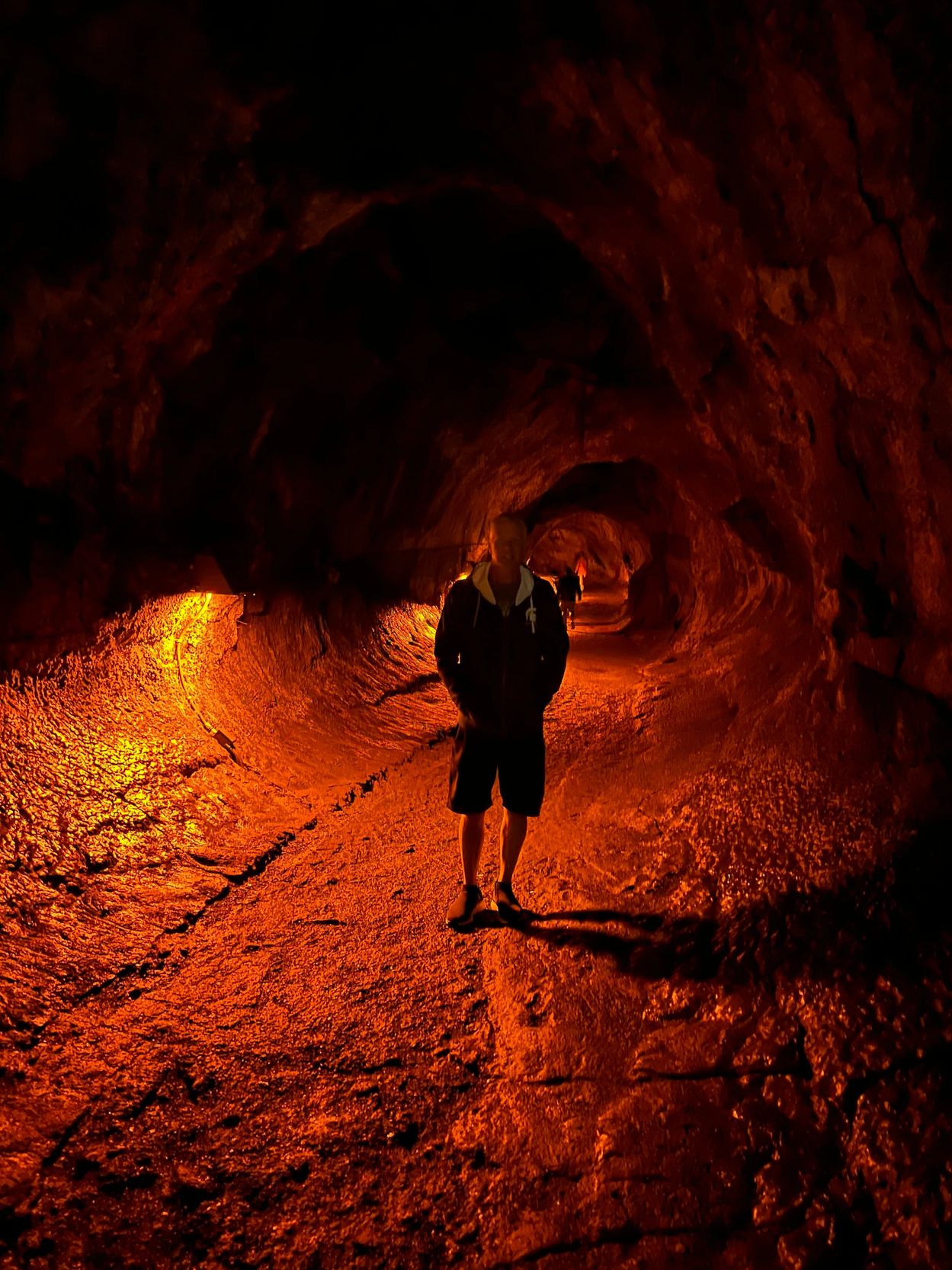 Person standing inside an orange-lit cave tunnel.