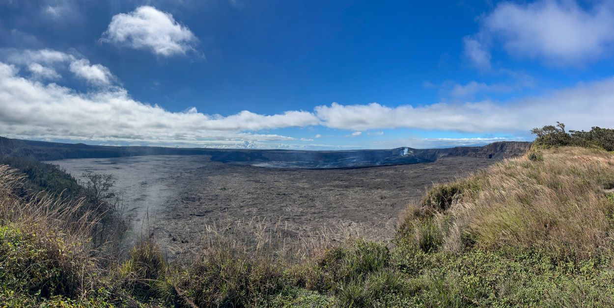 Vast volcanic crater under a partly cloudy blue sky.